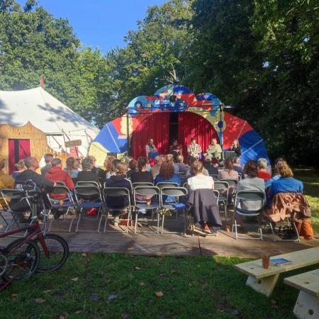 Uitwijken_inspiratiedag 2025 zicht op zittend publiek en buitenpodium, en een circustent